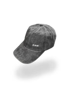 A washed dark gray baseball cap with a small white embroidered logo on the front, shown floating against a solid white background with a soft shadow underneath.