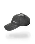 A dark gray washed cotton baseball cap with a small white embroidered logo on the front, shown against a plain white background with a soft shadow underneath.