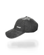 A dark gray washed cotton baseball cap with a small white embroidered logo on the front, shown against a plain white background with a soft shadow underneath.